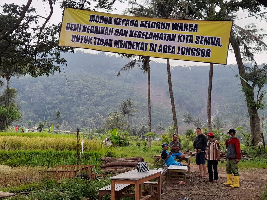 Sejumlah warga Desa Sumber Ngepoh, Kabupaten Malang, Jawa Timur, Minggu (13/3/2022), berjaga memantau kondisi lereng perbukitan longsor yang tampak jauh di belakang mereka.