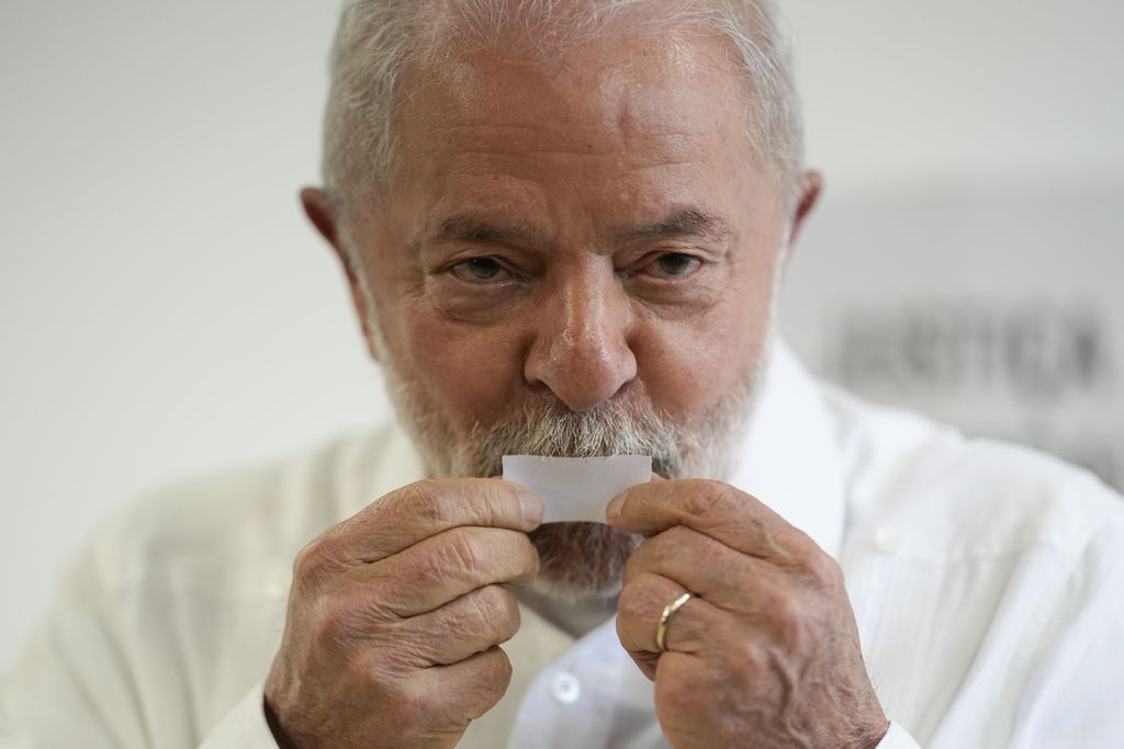 Luiz Inacio Lula da Silva tersenyum sambil mencium sebuah kertas sebelum menggunakan hak suaranya pada pemilihan presiden Brasil, 30 Oktober 2022.  