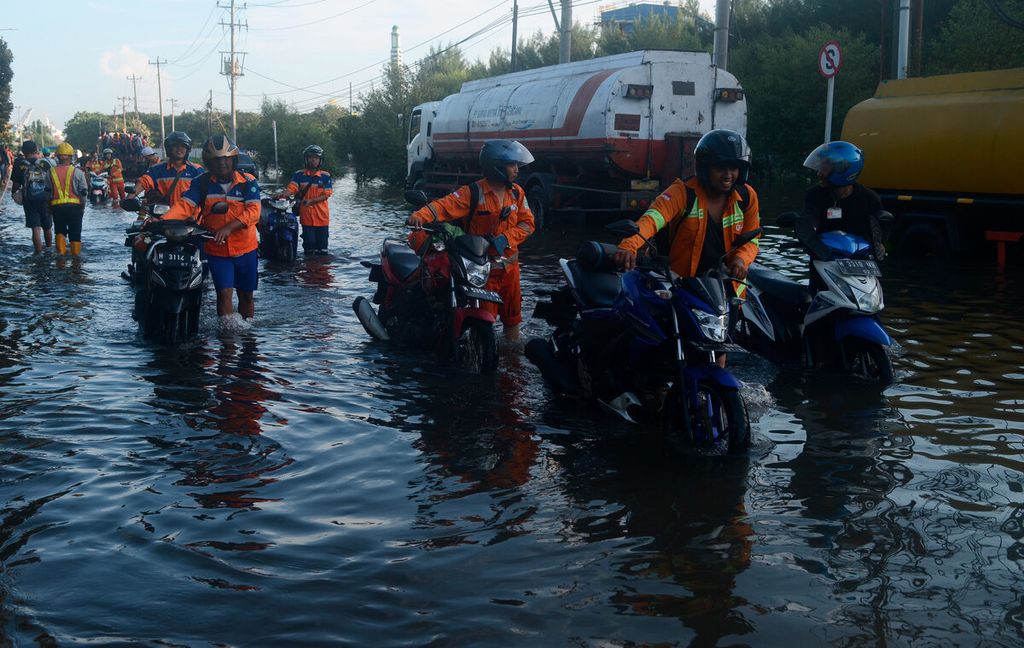  Workers push their motorbikes after they could not be rescued when tidal floods flooded the Tanjung Emas Port area in Semarang City, Central Java, Tuesday (24/5/2022).