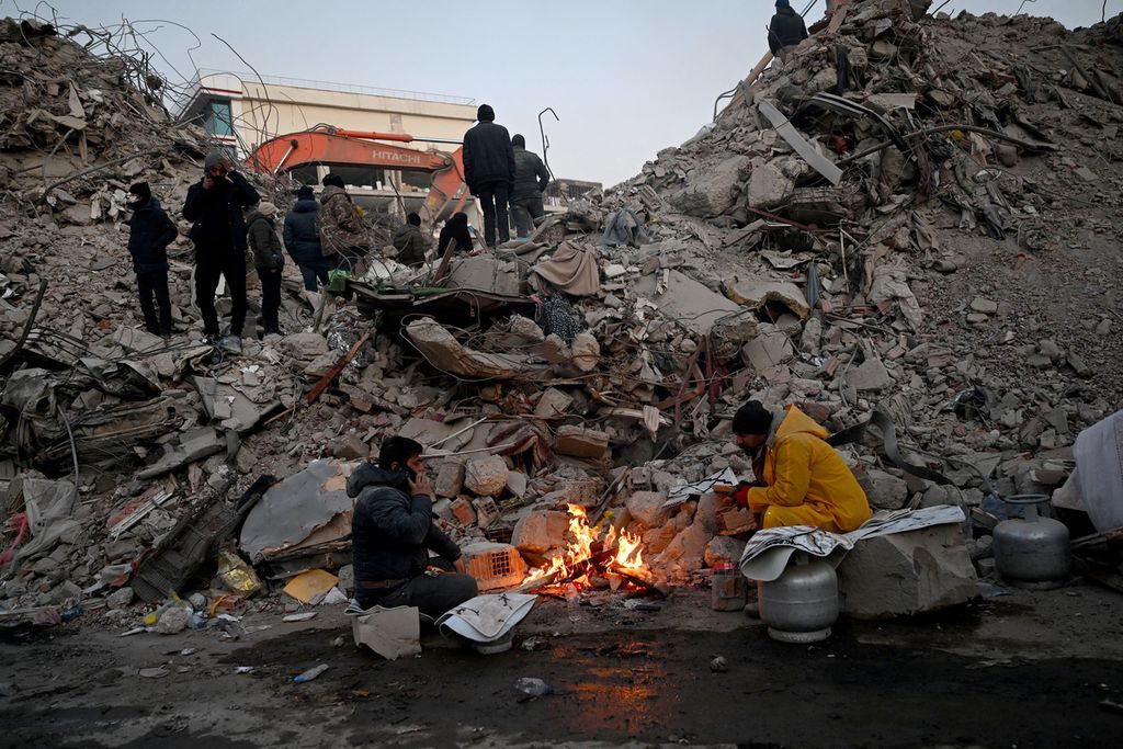 Sejumlah warga menghangatkan diri di dekat api unggun yang menyala di depan reruntuhan bangunan yang rusak akibat gempa, di Kahramanmaras, Turki, 12 Februari 2023. 