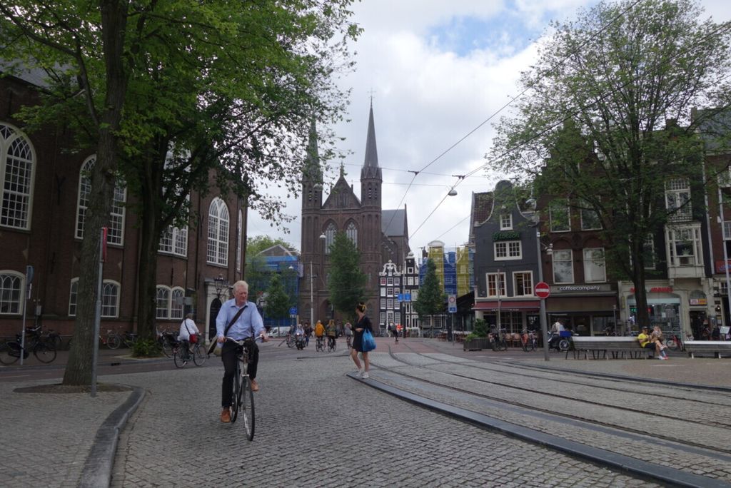 Pesepeda dan pejalan kaki melintas di jalan di Amsterdam, Belanda, suatu hari pada Juli 2019 lalu. Tampak jalur tram di ruas yang sama.