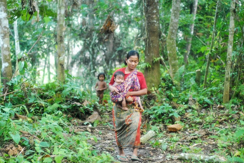 Induk Nidar membawa bayinya menuju tempat ritual memandikan anak di komunitas Orang Rimba di Taman Nasional Bukit Duabelas, Sarolangun, Jambi, Sabtu (2/7/2022).