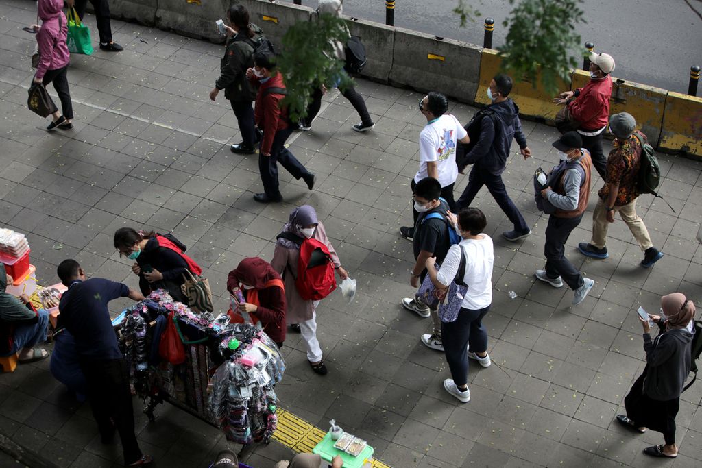 Pekerja sektor formal dan informal melintasi jalur pedestrian di Jalan Blora, Jakarta setelah keluar dari Stasiun Sudirman, 4 Januari 2022. Terbitnya Peraturan Pemerintah Pengganti Undang-undang atau Perppu Nomor 2 Tahun 2022 tentang Cipta Kerja menuai kritik baik dari pekerja maupun pengusaha. 