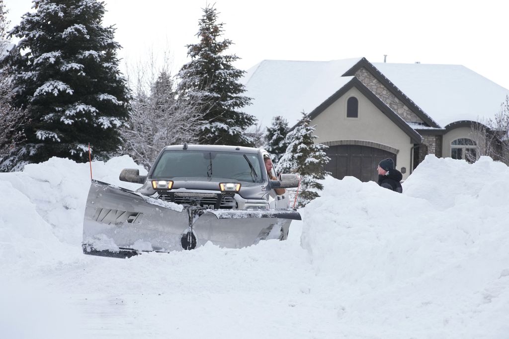 Pengemudi mobil penyapu salju berbicara kepada pemilik rumah saat membersihkan tumpukan salju di jalan permukiman di Draper, Utah, AS, 23 Februari 2023. 