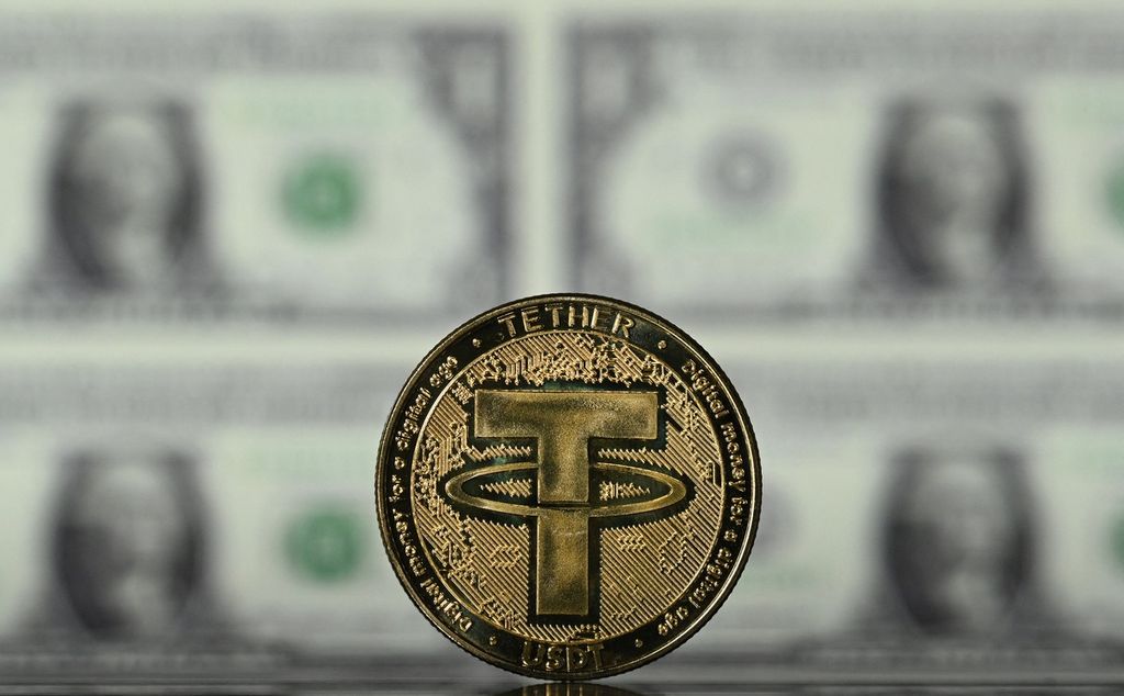 Ilustrasi koin suvenir uang kripto Tether, berlatar layar yang memperlihatkan uang kertas dollar AS. Tether (USDT) adalah token Ethereum yang merupakan <i>stablecoin</i>. 