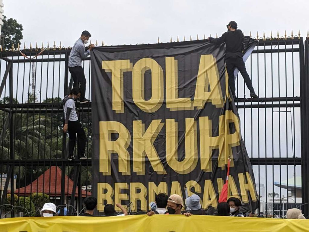 Dua peserta aksi penolakan RKUHP memasang spanduk di gerbang utama Kompleks DPR, Senayan, Jakarta Pusat pada Senin (5/12/2022).