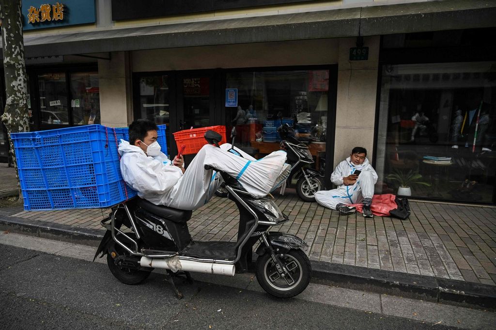 Seorang pekerja jasa pengantar barang, dengan memakai baju pelindung khusus, beristirahat di atas sepeda motornya di Distrik Jing'an yang tengah diberlakukan penguncian wilayah di Shanghai, China, Rabu (25/5/2022). 