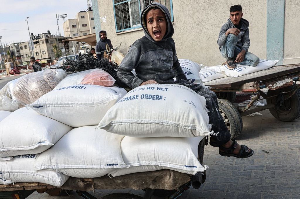 Seorang anak Palestina duduk di atas tumpukan karung berisi tepung yang diterima sebagai bantuan untuk keluarga-keluarga miskin di pusat distribusi  Badan Bantuan Sosial dan Pekerja Perserikatan Bangsa-Bangsa (UNRWA) di kamp pengungsi Rafah, Jalur Gaza selatan, 22 Januari 2022. 
