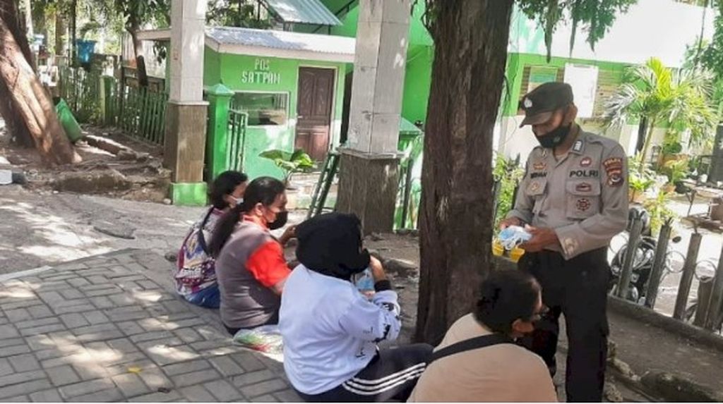 Seorang anggota Polda NTT melakukan sosialisasi penerapan protokol kesehatan kepada warga Kupang yang sedang nongkrong di jalan dan trotoar. Mereka membagikan masker kepada warga dan mengajak warga menjaga jarak.