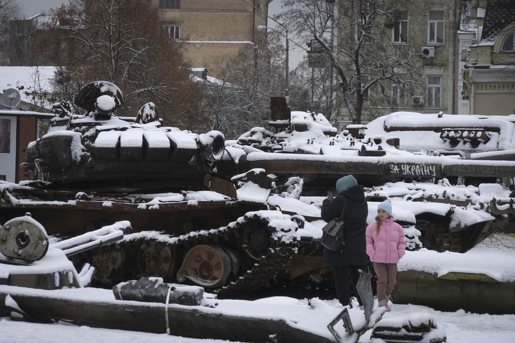 Seorang perempuan dan anak melihat sisa-sisa kendaraan militer Rusia yang rusak dan kini diselimuti salju di sebuah lokasi di Kota Kyiv, Ukraina, Senin (12/12/2022). 