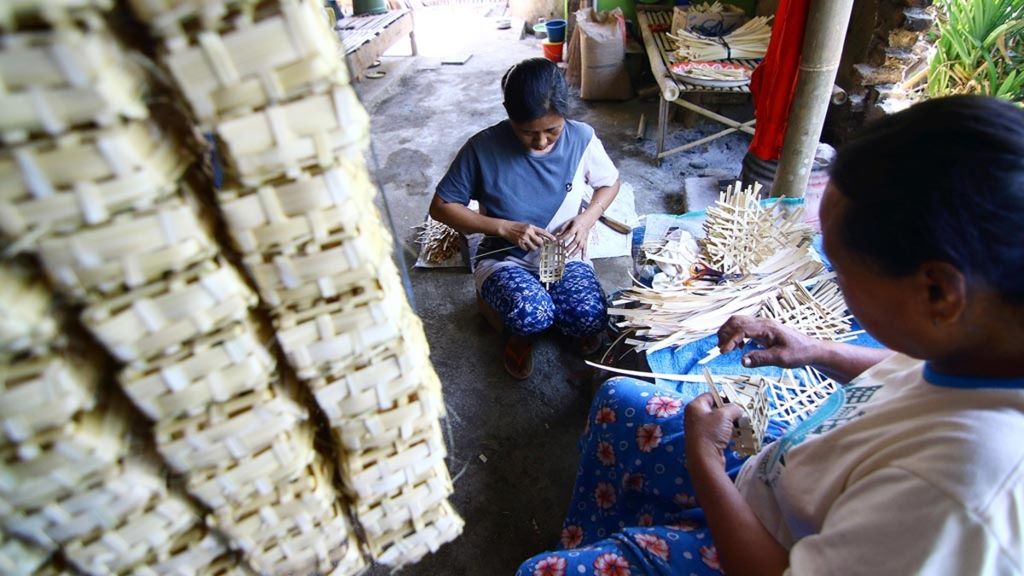 Zaenab (kiri) dibantu tetangganya, Kosiah, membuat <i>godhong </i>atau wadah ikan dari anyaman bambu di Dusun Krajan, Desa Kebaman, Kecamatan Srono, Banyuwangi, Selasa (9/10/2018). Dengan modal bambu seharga Rp 15.000, mereka mampu membuat 1.000 buah <i>godhong </i>hingga dihargai Rp 120.000.
