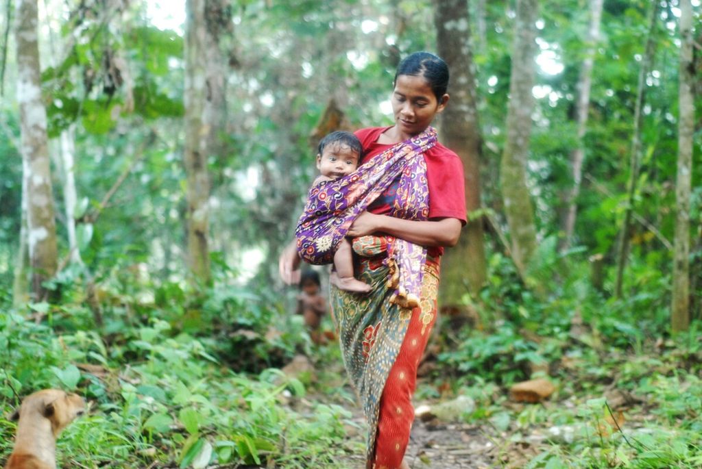 Induk Nidar membawa bayinya menuju tempat ritual memandikan anak di komunitas Orang Rimba di Taman Nasional Bukit Duabelas, Sarolangun, Jambi, Sabtu (2/7/2022).