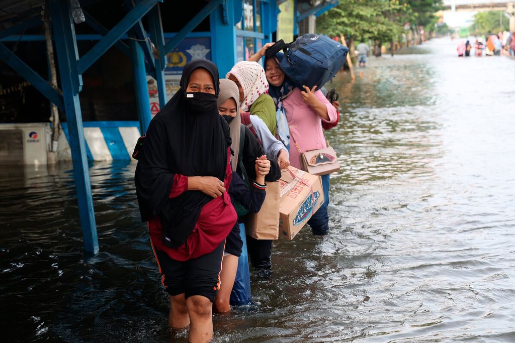 Warga berjalan melintasi banjir untuk mendapatkan transportasi yang akan mengantarkan mereka keluar kota dari Kaligawe, Kota Semarang, Jawa Tengah, Senin (2/1/2023).