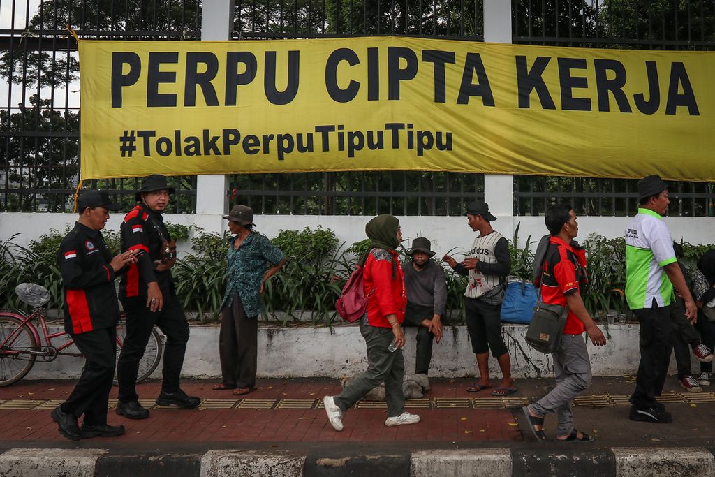 Peserta aksi melintasi spanduk penolakan Perppu Cipta Kerja di depan Gedung Parlemen, Jakarta, Selasa (28/2/2023). Ribuan massa yang terdiri dari buruh, mahasiswa, dan sejumlah elemen masyarakat menggelar aksi penolakan terhadap Peraturan Pemerintah Pengganti Undang-undang (Perppu) Nomor 2 Tahun 2022 tentang Cipta Kerja.