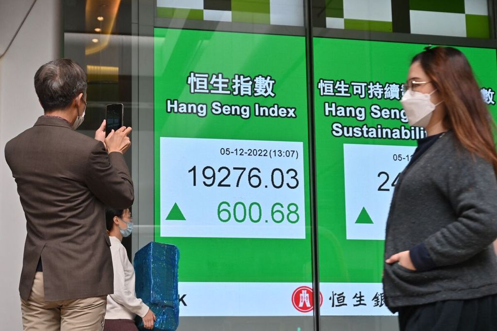 Pejalan-pejalan kaki berjalan melintas di depan papan elektronik yang memperlihatkan index Han Seng di Hong Kong, Senin (5/12/2022).
