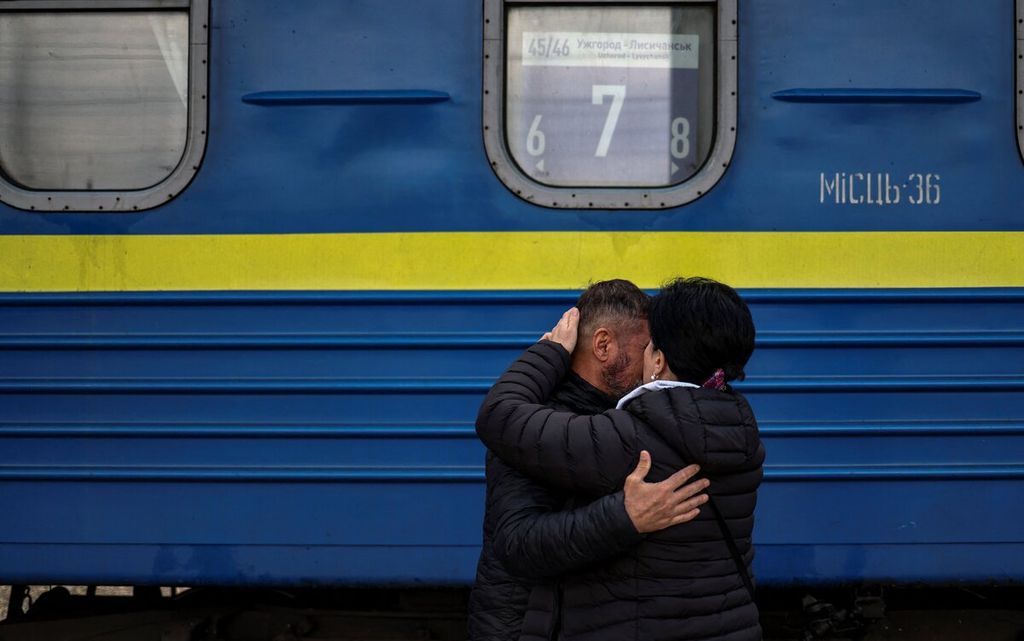 Seorang pria memeluk isterinya yang akan naik kereta di Stasiun Pusat Slovyansk di wilayah Donbass, 12 April 2022,.  (Photo by RONALDO SCHEMIDT / AFP)
