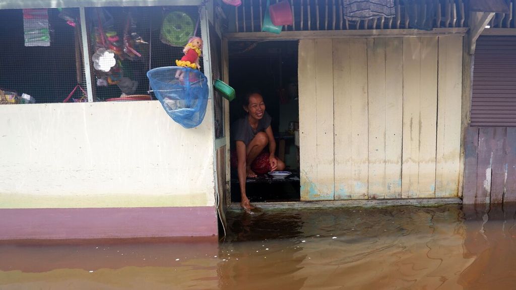 Seorang warga mencuci piring di teras depan rumahnya di Desa Sungai Lulut, Kecamatan Banjarmasin Timur, Kota Banjarmasin, Kalimantan Selatan, Minggu (24/1/2021). Hampir dua pekan pemukiman penduduk di bantaran Kali Lulut, anak Sungai Martapura, terendam banjir dan air belum juga surut.