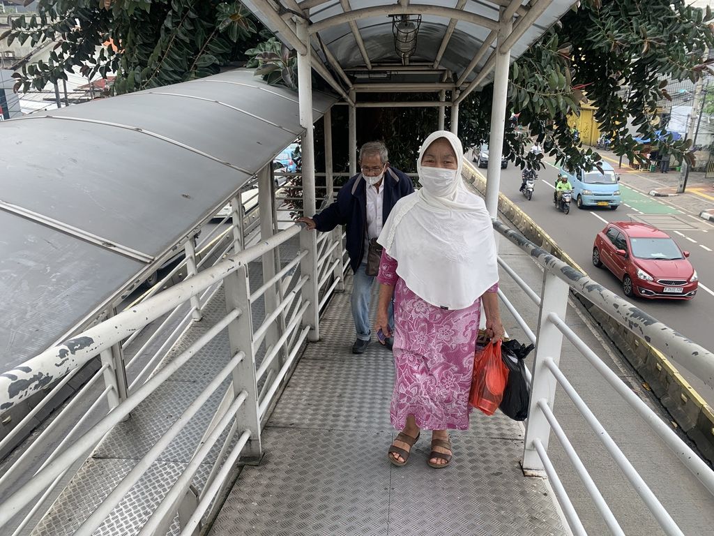 Amina (depan) dan Ranil (belakang), dua warga lansia yang sedang melewati jembatan penyeberangan orang atau JPO, seusai keluar dari Halte Transjakarta Bidara Cina, Jakarta Timur, Rabu (15/3/2023).
