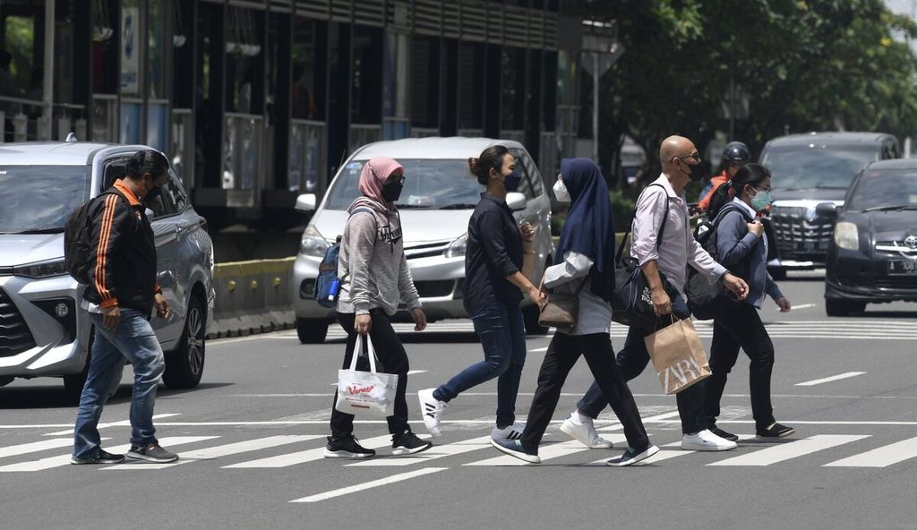 Sejumlah pekerja kantoran menyeberang di Jalan Sudirman menuju ke tempat kerja di kawasan Sudirman, Jakarta, Senin (21/2/2022).