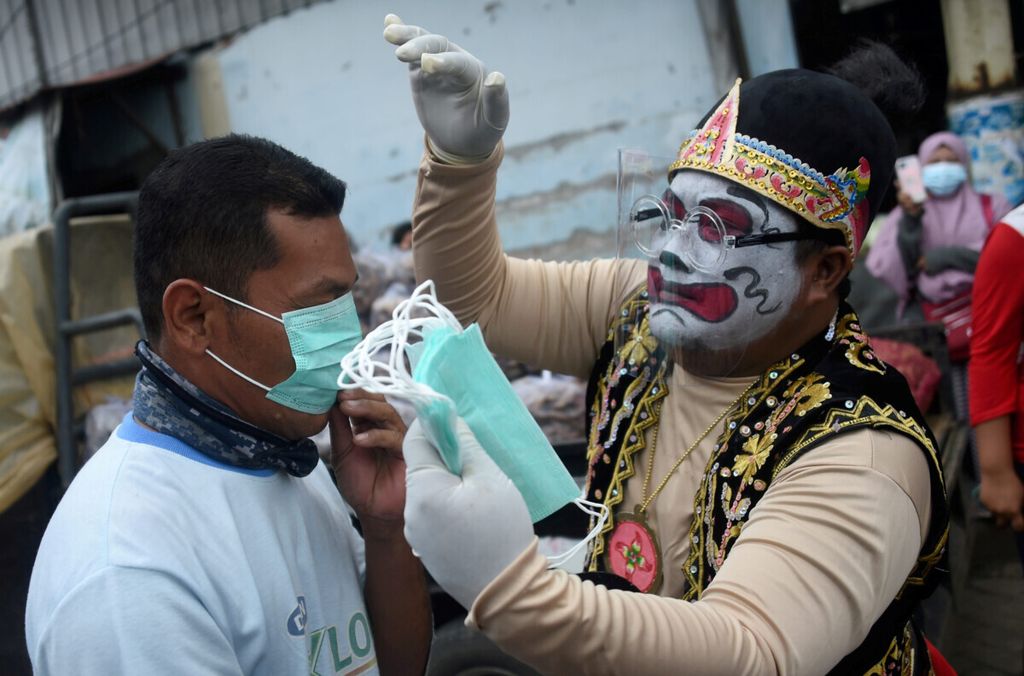 Petugas yang menggunakan busana punakawan memasangkan masker medis kepada pedagang saat kampanye patuh pada protokol kesehatan di Pasar Porong, Sidoarjo, Jawa Timur, Jumat (5/2/2021). Kegiatan yang diselenggarakan oleh Polresta Sidoarjo ini bertujuan mengajak masyarakat untuk tetap patuh menjalani protokol kesehatan. 