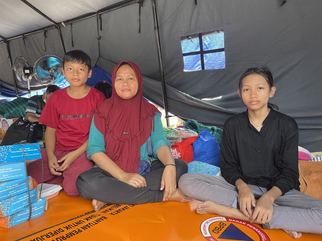 Yuli Yarsi (45) berfoto bersama kedua anaknya, Michaelia Shahada (kanan) dan Nasyat Hazel Josevan, saat ditemui di posko pengungsian PMI Jakarta Utara, Senin (6/3/2023). Michaelia dan Hazel merupakan murid SD Unwanus Saadah, Koja.