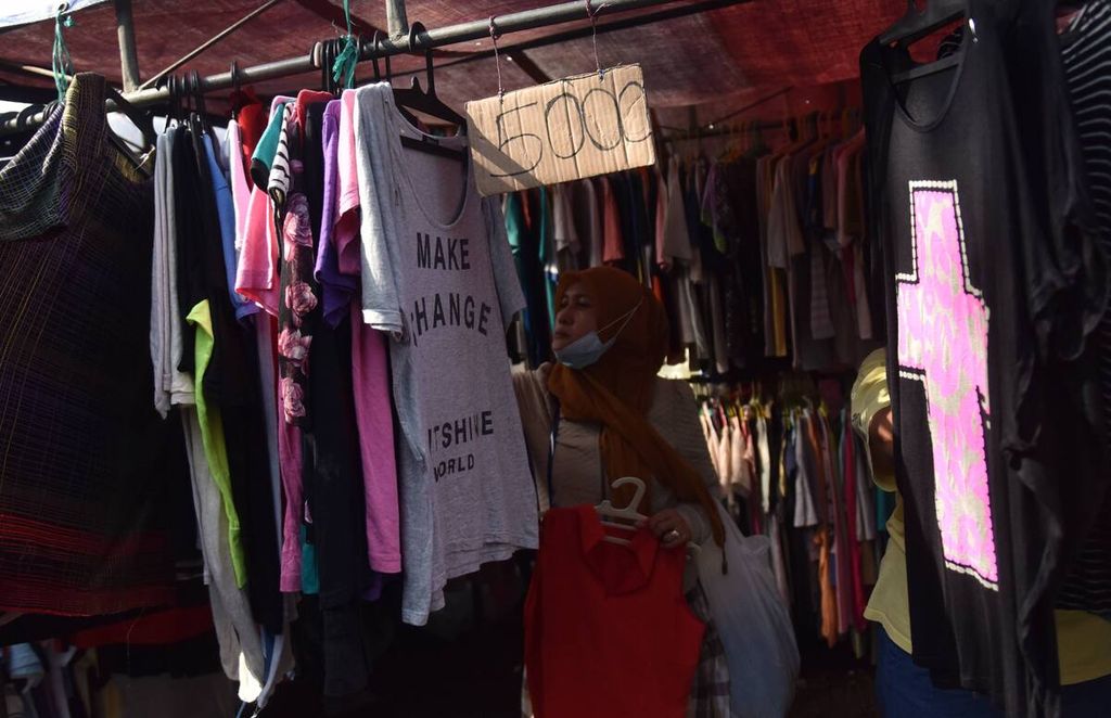 Warga membeli kaus di Pasar Pagi Tugu Pahlawan, Kota Surabaya, Jawa Timur, April 2022. Pasar pagi yang berlangsung setiap hari Minggu tersebut didominasi penjual pakaian bekas impor. 