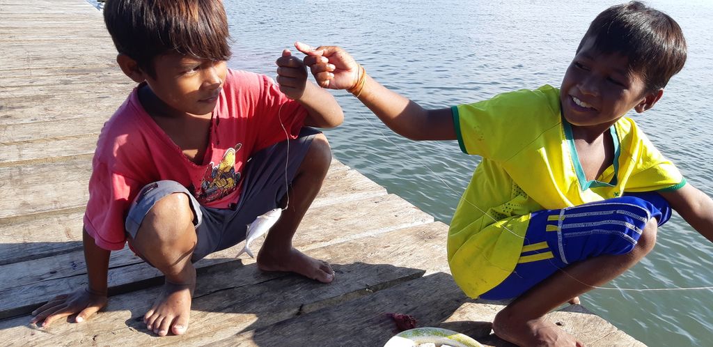 Dua anak nelayan Desa Sangowo, Kecamatan Morotai Timur, Kabupaten Pulau Morotai, Maluku Utara, tersenyum mengangkat ikan kecil hasil tangkapan, Rabu (27/7/2022).
