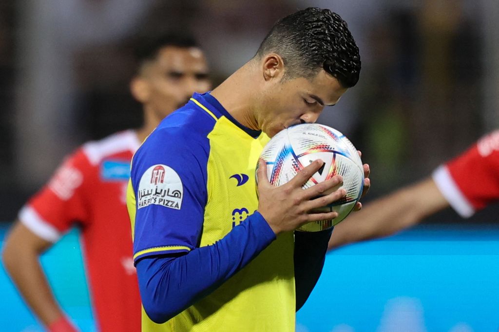 Penyerang Al Nassr, Cristiano Ronaldo, mencium bola sebelum mengeksekusi tendangan penalti dalam pertandingan Liga Arab Saudi antara Al Wehda dan Al Nassr, Jumat (10/2/2023) dini hari WIB, di Stadion Raja Abdul Aziz, Mekkah. Ronaldo mencetak 4 gol dalam pertandingan tersebut. 