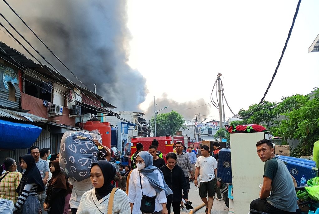 Residents went back and forth carrying goods and away from the dense black smoke that enveloped residents' settlements in RW 003 Jalan Kapuk Utara 2, Kapuk Muara, Penjaringan, North Jakarta, which was burnt to the ground, Sunday (30/7/2023).