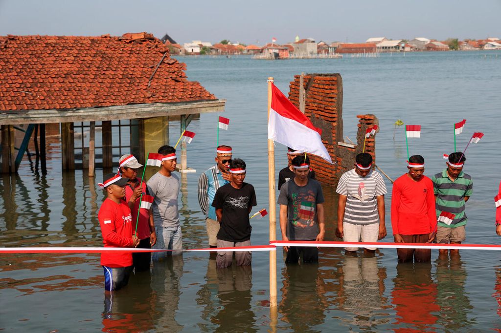 Warga mengikuti upacara HUT ke-77 RI dengan latar belakang sebuah rumah yang tenggelam di Dukuh Timbulsloko, Desa Timbulsloko, Kecamatan Sayung, Kabupaten Demak, Jawa Tengah, Rabu (17/8/2022).