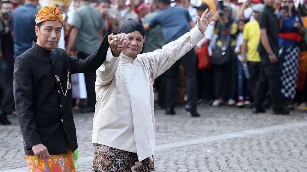 Joko Widodo (kiri) dan Prabowo Subianto bergandengan tangan saat berjalan menuju tempat duduk seusai Deklarasi Kampanye Damai Pemilu Serentak 2019 di Lapangan Monumen Nasional, Jakarta, Minggu (23/9/2018). Pasangan capres-cawapres menaruh harapan dari dukungan para sukarelawan saat partai koalisi juga harus berkonsentrasi menghadapi pemilu legislatif.
