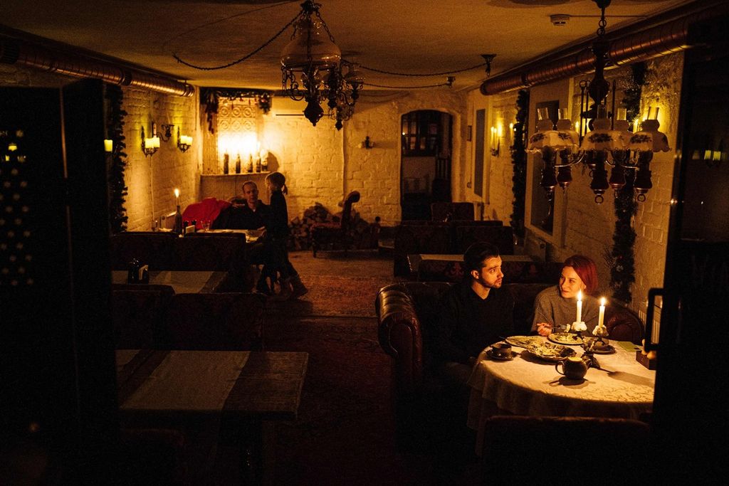 Sepasang laki-laki dan perempuan menikmati santap malam di sebuah restoran yang diterangi dengan lampu lilin menyusul pemadaman listrik di pusat kota Kyiv, Ukraina, Selasa (6/12/2022). 