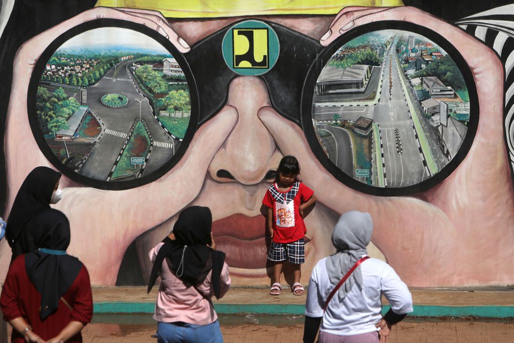 Pengunjung berfoto dengan latyar belakang mural yang menghiasi salah satu tembok di Taman Kota 2 BSD, Tangerang Selatan, Banten, Minggu (8/5/2022). Pada libur Lebaran seperti saat ini, taman kota yang baru selesai direvitalisasi dan dipercantik ini menjadi salah satu lokasi favorit warga Tangerang Selatan untuk jalan-jalan bersama keluarga atau sekadar olahraga. 