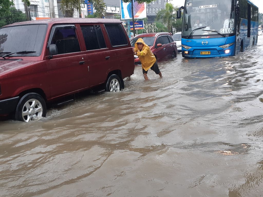 Seorang warga membantu mendorong mobil yang mogok akibat banjir di Jalan R Soekamto, Palembang, Sumatera Selatan, Sabtu (25/12/2021). Banjir disebabkan intensitas hujan yang tinggi dan pasangnya air sungai.