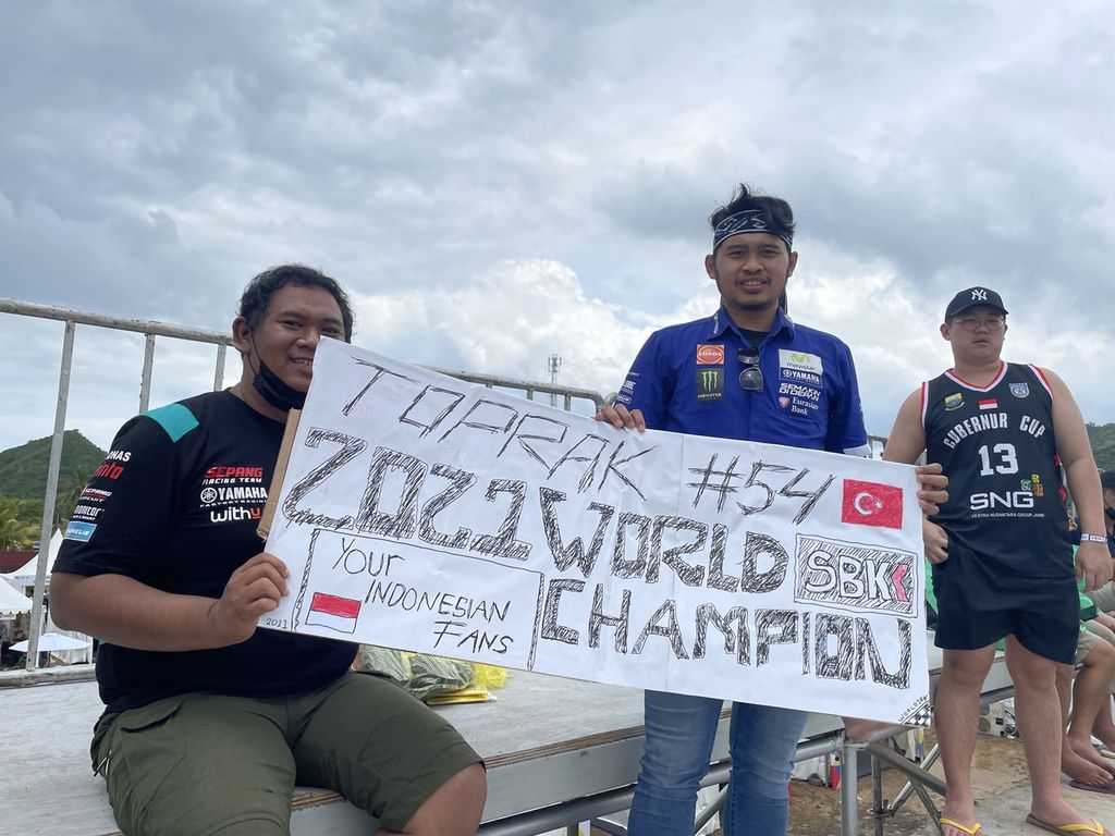Penggemar Toprak Razgatlioglu, pebalap tim Pata Yamaha With Brixx, membawa poster bertuliskan ”Toprak #54, 2021 World Superbike Champion” saat menyaksikan <i>race</i> 1 Kejuaraan Dunia Superbike di Sirkuit Internasional Jalan Raya Pertamina Mandalika, Kuta, Pujut, Lombok Tengah, Nusa Tenggara Barat, Minggu (21/11/2021). Meski cuaca tidak bersahabat, penonton tetap antusias menyaksikan balapan hingga selesai.