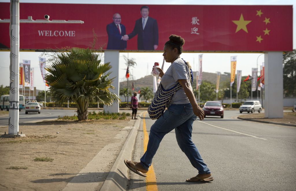 Seorang perempuan menyeberang jalan di dekat papan reklame berisi ucapan sambutan atas kunjungan kenegaraan Presiden China Xi Jinping di Port Moresby, Papua Niugini, 15 November 2018. 