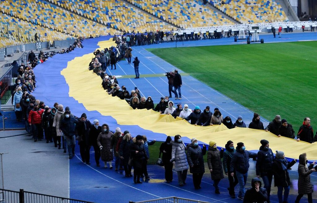 Warga membawa bendera Ukraina raksasa di Stadion Olimpiade, Kiev, untuk merayakan Hari Perasatuan pada 16 Februari 2022. Komunitas sepak bola Eropa dan dunia mengecam serangan militer Rusia ke Ukraina yang dimulai Kamis (24/2/2022).  