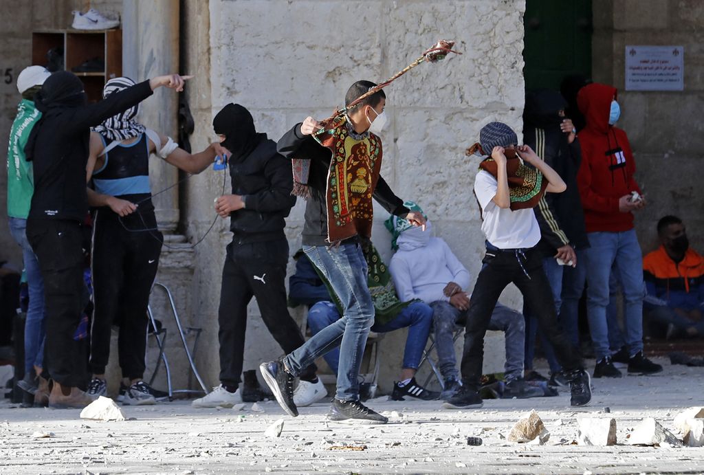 Sejumlah pemuda Palestina melempari aparat keamanan Israel dengan batu ketika kedua belah pihak bentrok, Jumat (22/4/2022). Liga Arab mengecam tindakan aparat keamanan Israel yang mengizinkan warga Yahudi beribadah di kompleks Masjid Al Aqsa sebagai tindakan yang provokatif dan ilegal. 