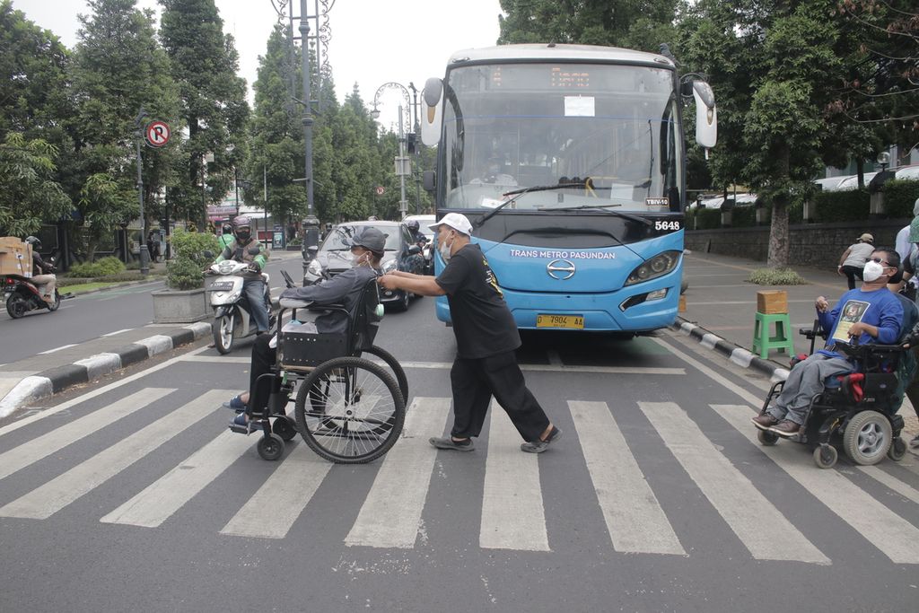 Sejumlah pengguna kursi roda melintasi lampu merah perempatan Dago-Cikapayang, Kota Bandung, Jawa Barat, Selasa (1/3/2022). Saat melintas, mereka butuh bantuan dari sejumlah orang karena jalur yang tidak rata dan berbatu.