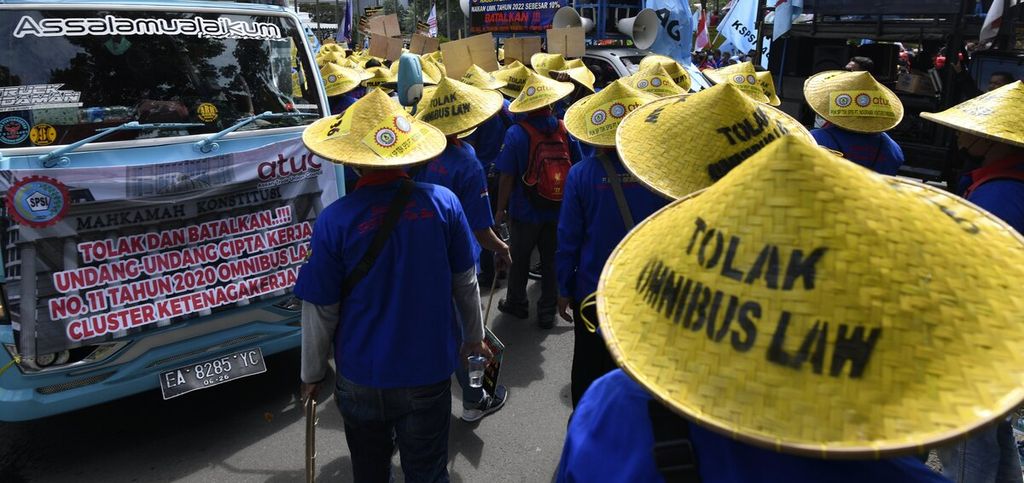 Buruh memakai caping bertuliskan ”Tolak Omnibus Law” saat massa buruh dari berbagai elemen menggelar aksi unjuk rasa sambil menunggu hasil putusan sidang Mahkamah Konstitusi terkait UU Cipta Kerja di Jakarta, Kamis (25/11/2021).