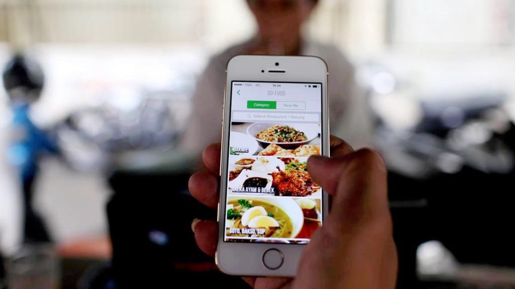 Warga mencoba memanfaatkan aplikasi pesan dan antar makanan yang diluncurkan Gojek melalui ponsel pintarnya di kawasan Bundaran Hotel Indonesia, Jakarta.