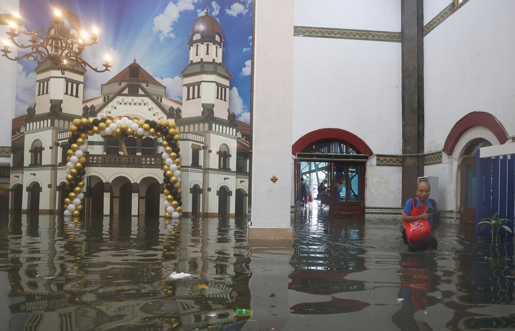 Penumpang kereta api melintasi banjir yang menggenangi ruang tunggu di Stasiun Tawang, Kota Semarang, Jawa Tengah, Sabtu (31/12/2022). Intensitas hujan yang tinggi dengan durasi lebih dari 5 jam tersebut menyebabkan bencana banjir di sejumlah wilayah Kota Semarang. Banjir yang melanda tersebut menghentikan hampir sebagian fasilitas publik. 