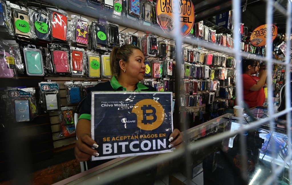 Seorang pedagang menunjukkan tanda bertuliskan menerima pembayaran dengan bitcoin di sebuah toko di San Salvador pada 26 Januari 2022. El Salvador adalah salah satu negara pertama yang secara resmi menggunakan bitcoin sebagai alat pembayaran yang sah. 