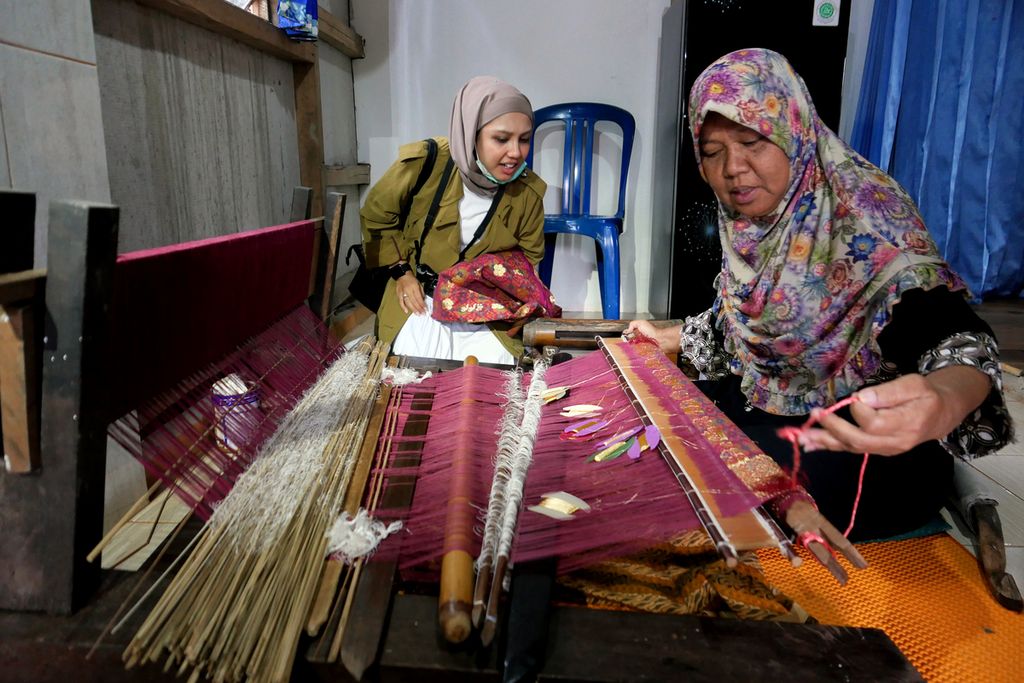Wisatawan asal Banda Aceh, Tia Rarani (26), mengamati penenun songket, Cek Ery (54), yang sedang menyelesaikan songket limar pesanan butik dari Jambi di belakang rumahnya di kawasan Ki Gede Ing Suro, Palembang, Sumatera Selatan, Rabu (13/1/2021). 
