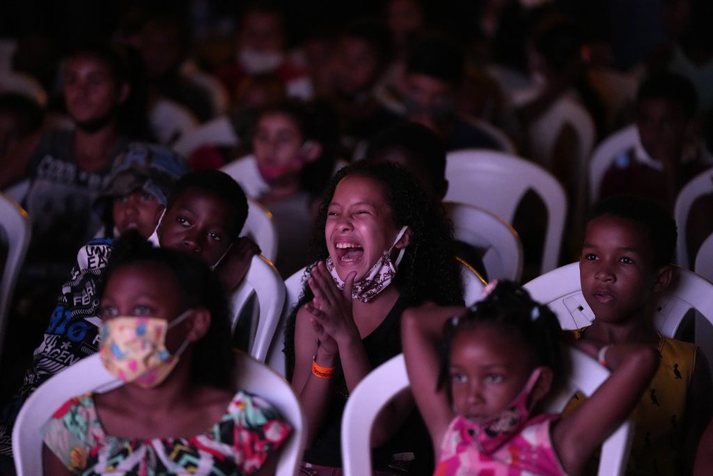 Anak-anak menonton film <i>Cinema no Morro</i> atau proyek bioskop di atas bukit di pusat budaya favela Vila Cruzeiro, Rio de Janeiro, Brasil, Senin (13/9/2021) waktu setempat. Mereka antusias menyaksikan film yang diputar di bioskop dadakan itu. 
