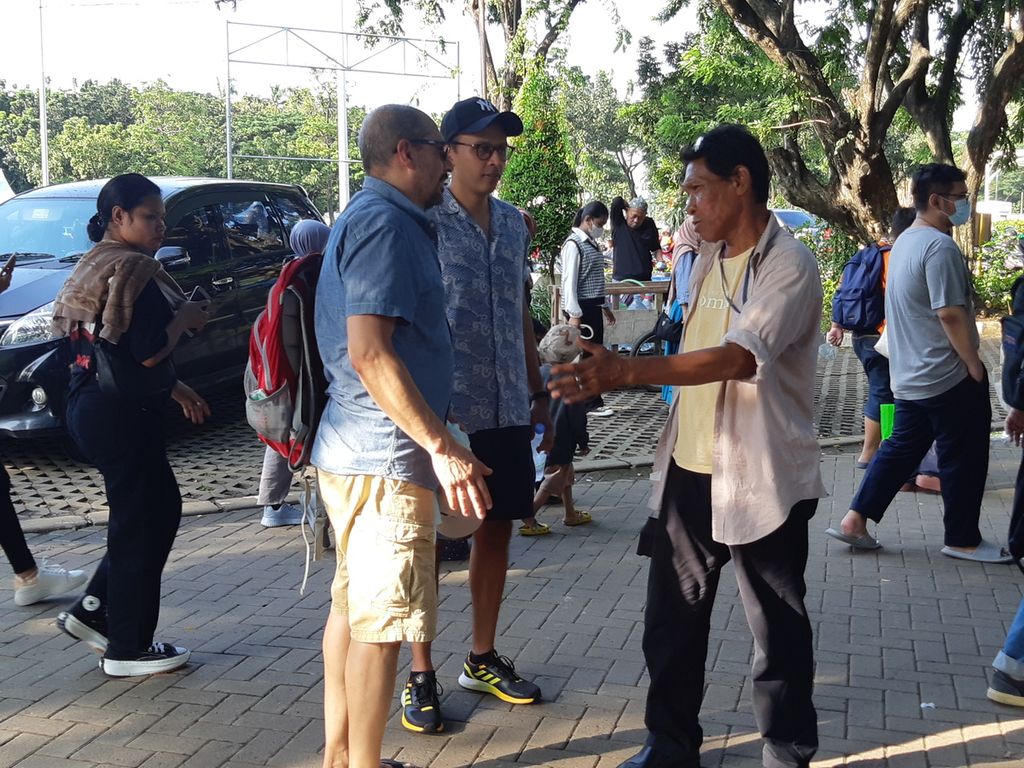  Sirul (58), pedagang suvenir, tengah berbincang dengan turis mancanegara di lapangan parkir IRTI Monas, Jakarta Pusat, pada Sabtu (18/3/2023).