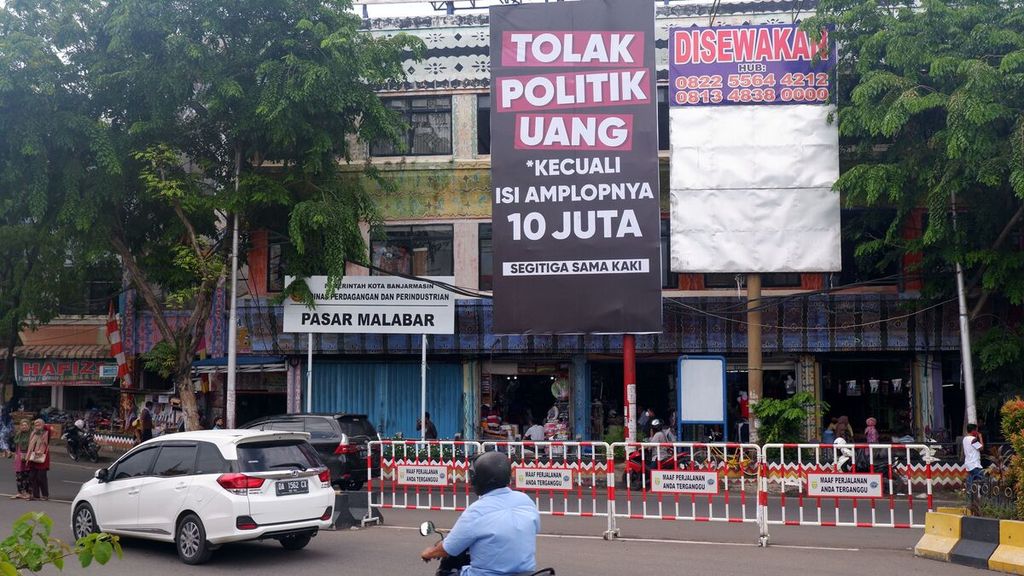 Baliho ajakan menolak politik uang bernada satire terpasang di sudut salah satu pasar di Kota Banjarmasin, Kalimantan Selatan, sehari menjelang pemungutan suara pemilihan kepala daerah serentak 2020, Selasa (8/12/2020). Pada 9 Desember, warga Banjarmasin akan memilih gubernur dan wali kota periode 2021-2024.