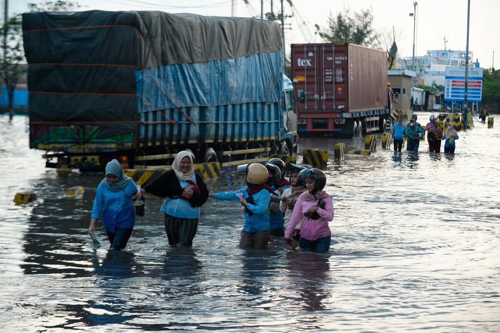 Pekerja pabrik melintasi banjir pasang air laut yang menggenangi akses jalan utama menuju Pelabuhan Tanjung Emas, Kota Semarang, Jawa Tengah, Senin (20/6/2022).