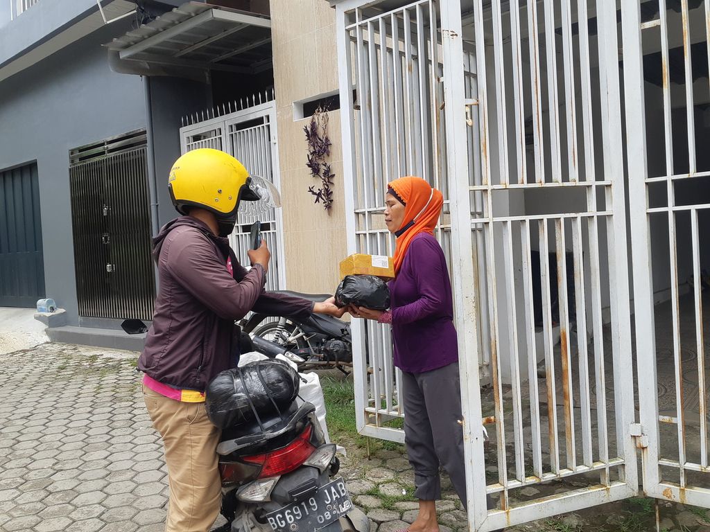 Aji Akbar (27) memberikan paket kepada salah satu pelanggan di Jalan Mayor Ruslan, Palembang, Sumatera Selatan, Selasa (7/3/2023). Aji merupakan salah satu pejuang paket di Palembang yang kerap membantu masyarakat mengantar paket.