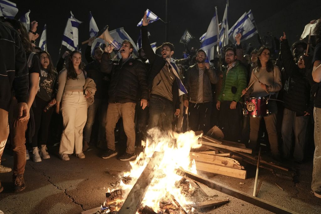 Para pendemo menentang reformasi hukum yang didorong Perdana Menteri Israel Benjamin Netanyahu mengelilingi api unggun sebagai ungakapan protes  di Tel Aviv, Minggu (26/3/2023) malam. 